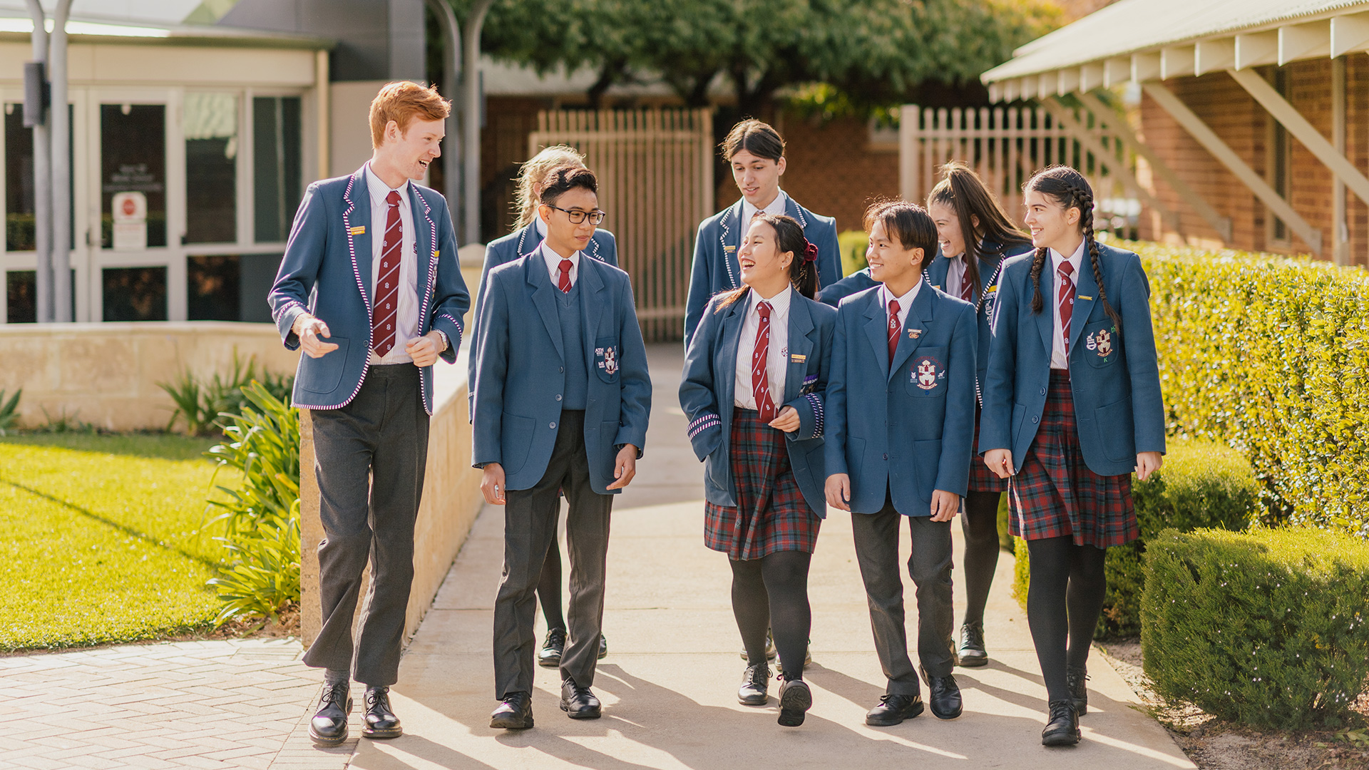 Pictured are a group of students walking, as they walk they chat amongst each other with smiles on their faces.
