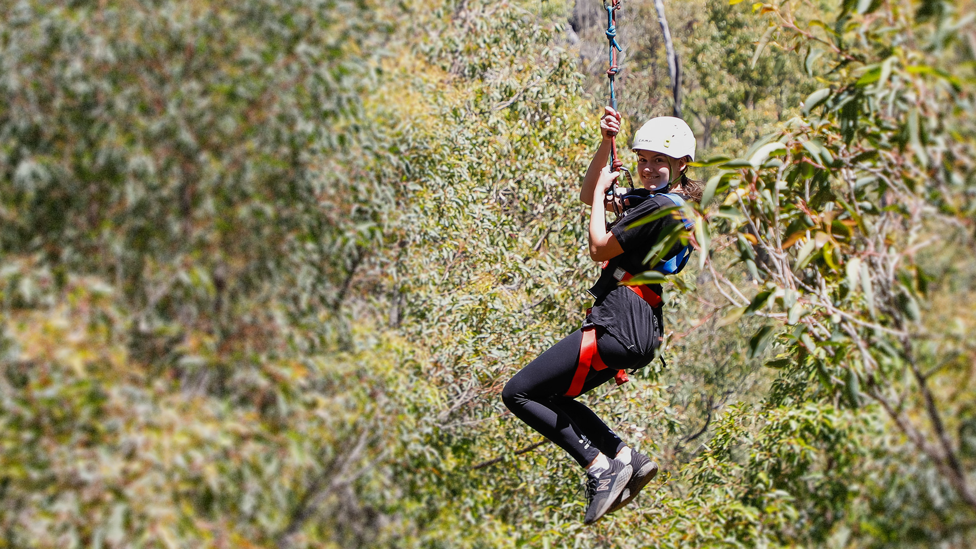 Pictured is a young girl on a flying fox suspended mid air. Surrounding her is greenery.