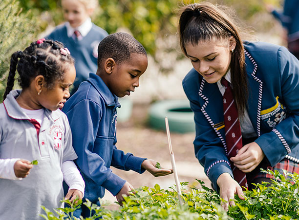 Pictured is an older student working with two younger students as they explore the herb garden.