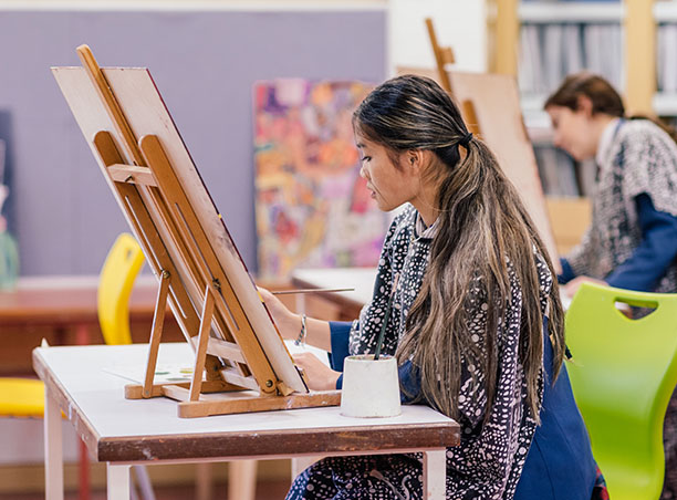 Pictured is a young woman painting at an easel.