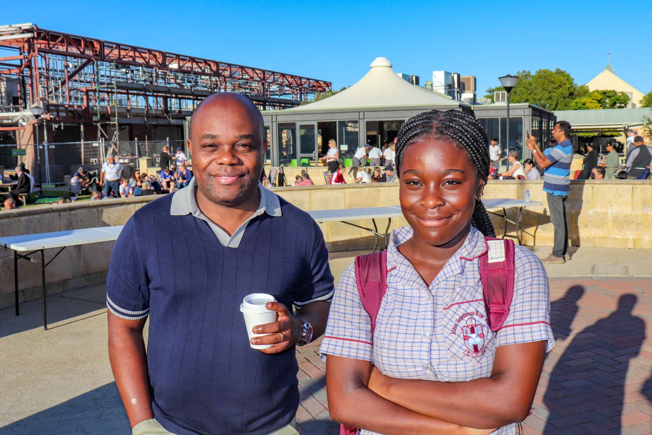 Pictured is a father and daughter at The Rite Journey Call and Departure Ceremony. The father holds a coffee, whilst his daughter smiles arms folded.